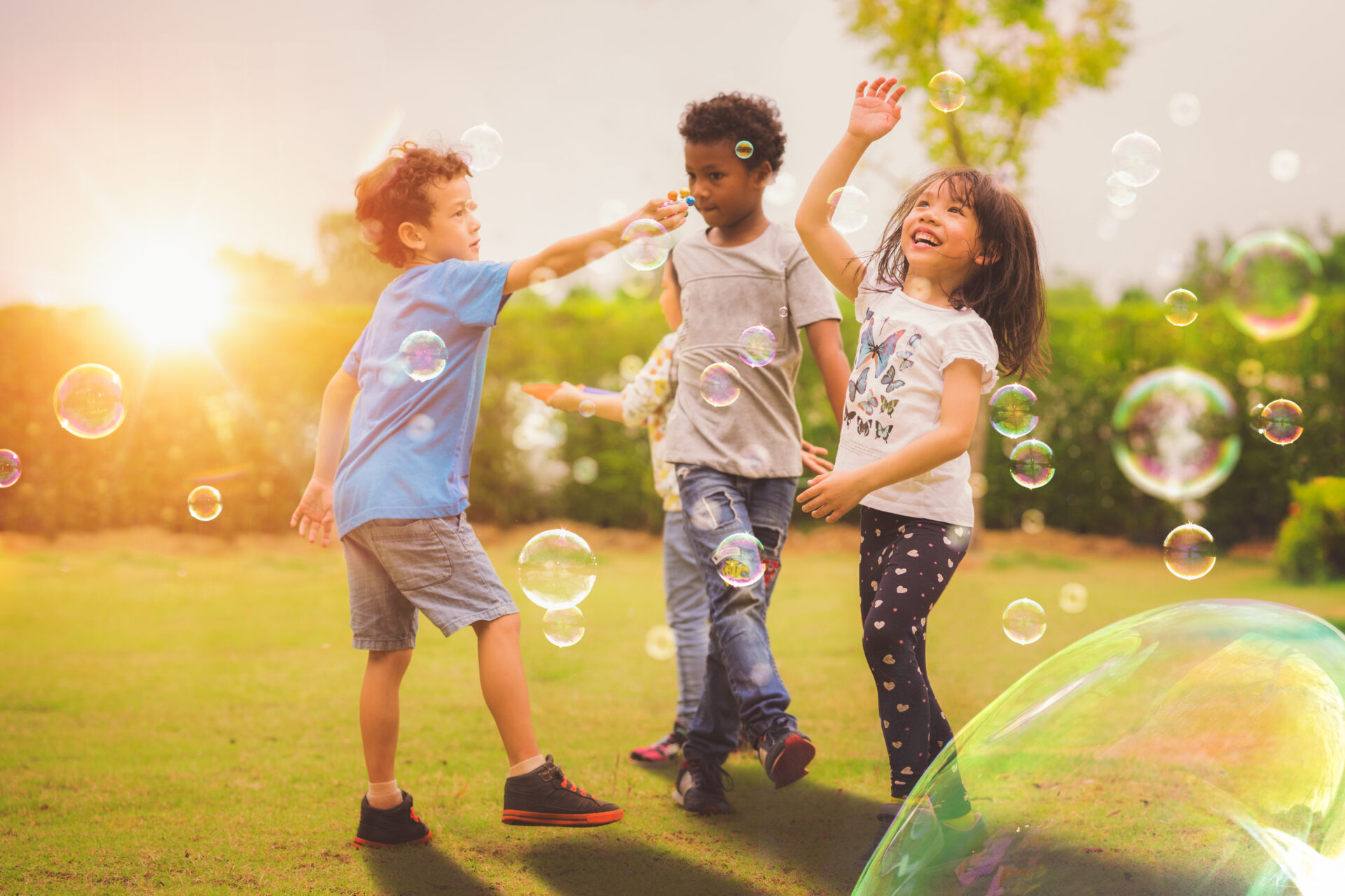 three children playing with soap bubbles in the grass